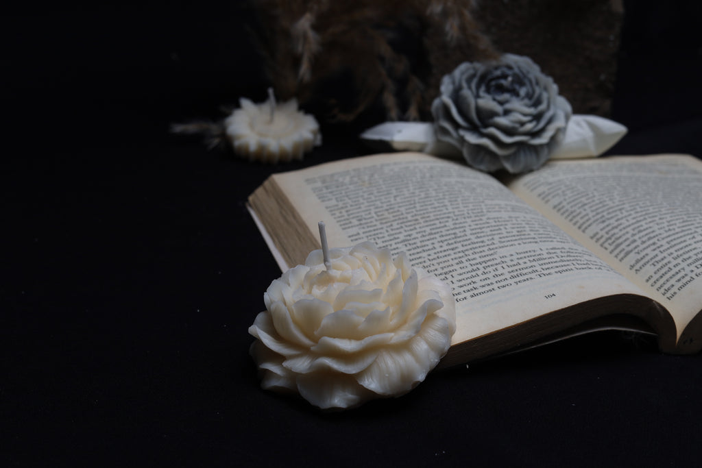 A set of white rose flower candles placed on an open book, with a dark background.