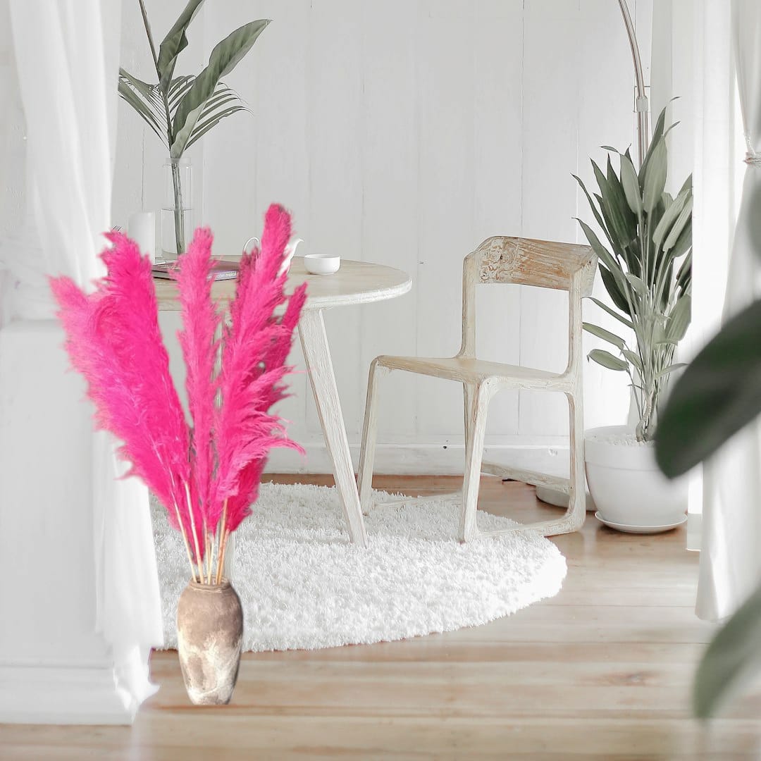 A bundle of Sorcish flamingo-pink pampas grass in a clear vase, with a fluffy, plume-like appearance, set against a home decor background.