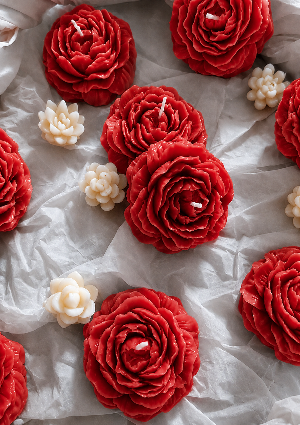 Red and white rose-shaped candles on a white fabric background