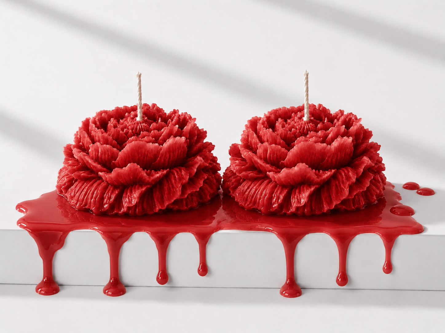 Two red rose-shaped candles on a white cake with red candle wax dripping.
