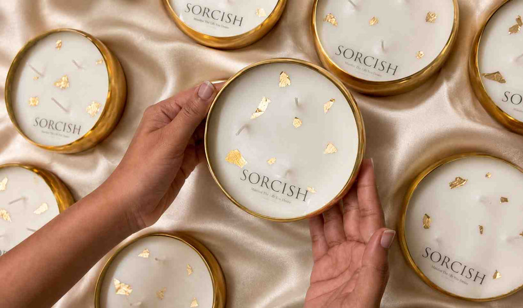 Hands holding a Sorcish product with other similar products in the background on a satin surface.