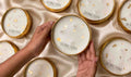 Hands holding a Sorcish product with other similar products in the background on a satin surface.