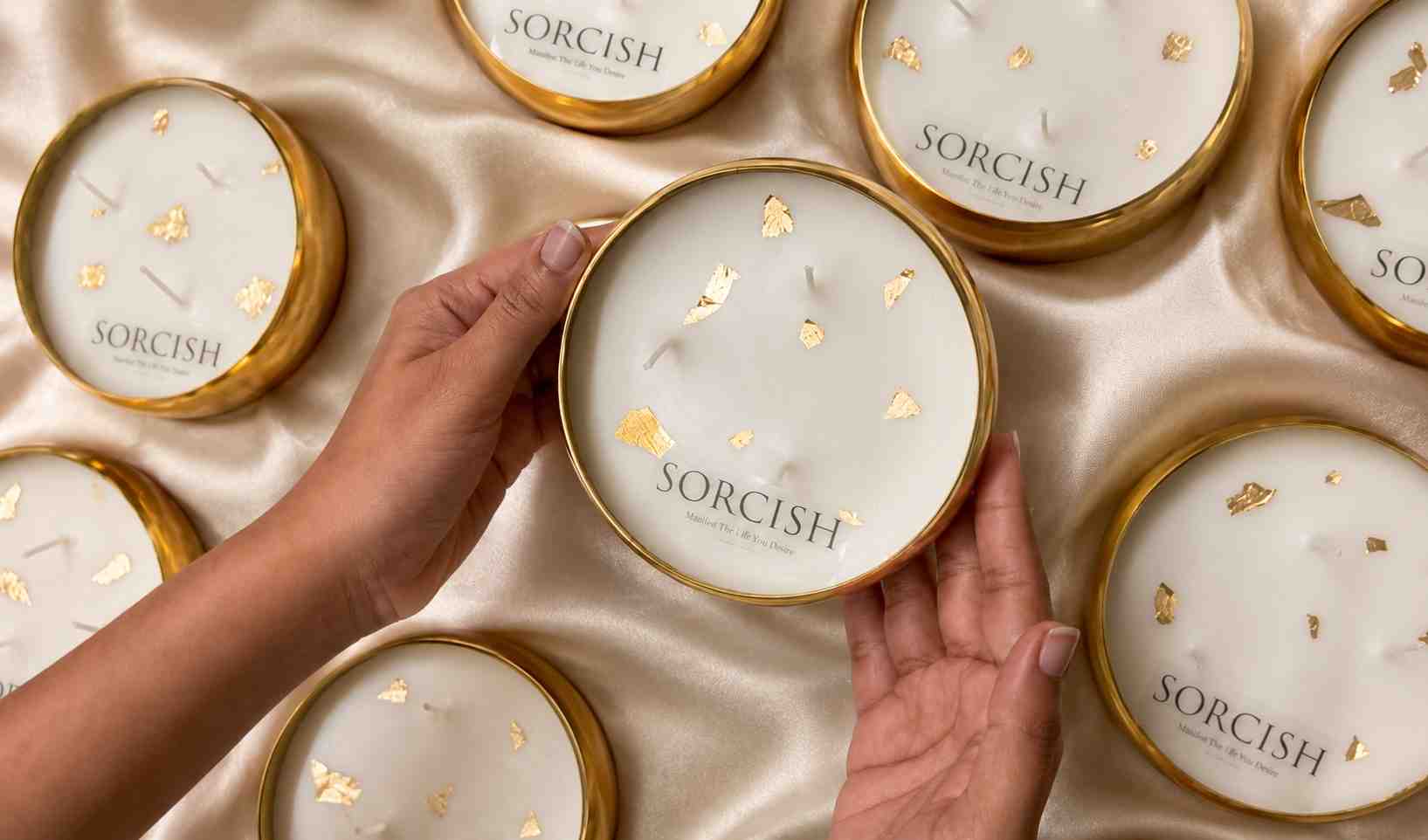 Hands holding a Sorcish product with other similar products in the background on a satin surface.