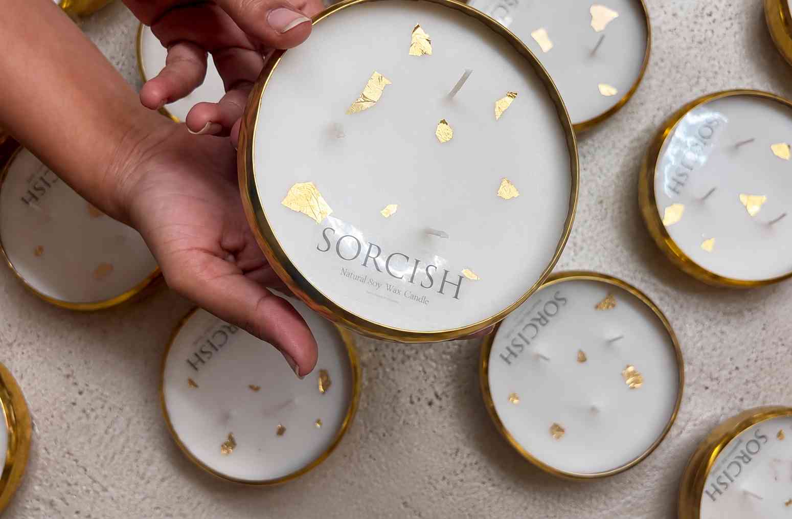 Hand holding a Sorcish candle among other similar candles on a textured surface