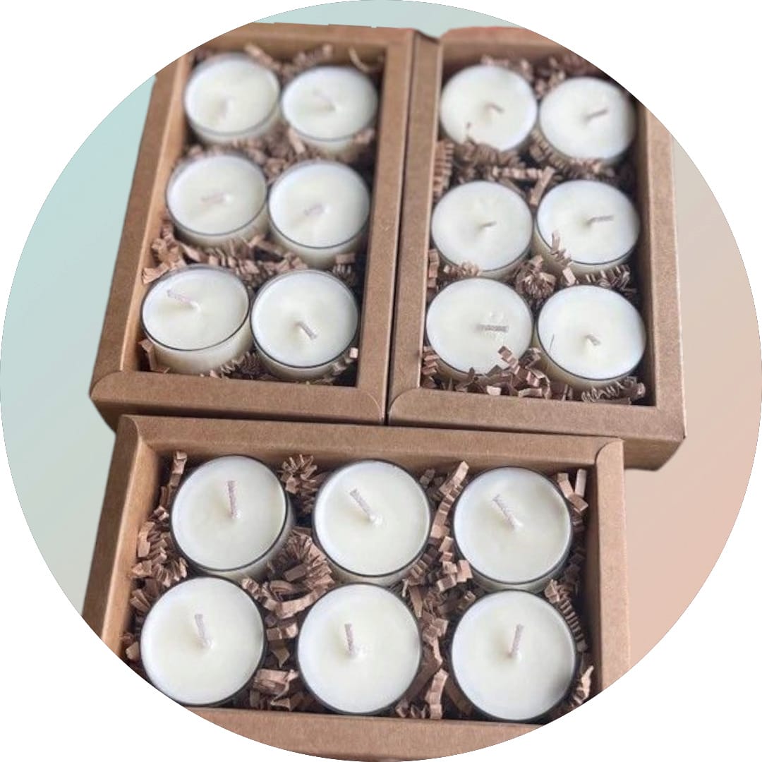 A set of white, round, scented candles in glass votive holders, arranged in three cardboard boxes with each other.
