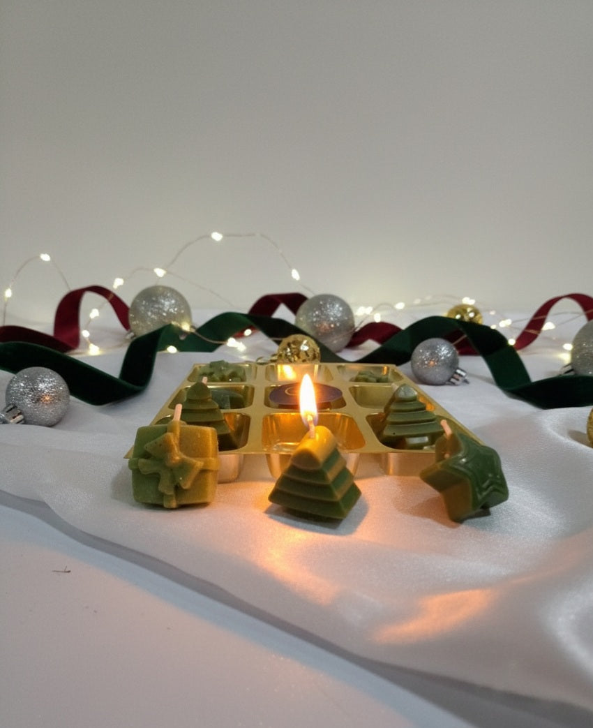 Decorative Christmas scene with green tree-shaped candles, red ribbon, and silver ornaments on a white surface.