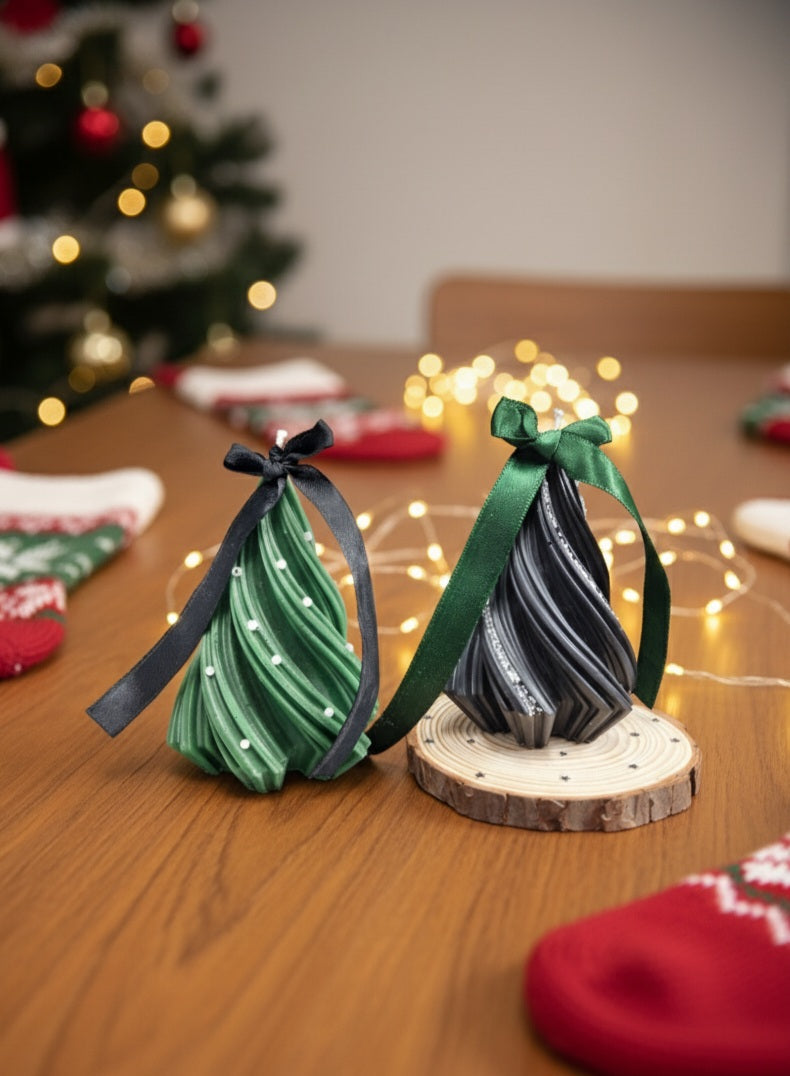 Two green paper Christmas trees on a wooden stand with a blurred festive background.