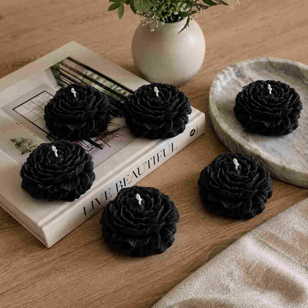 Black rose-shaped candles on a wooden surface with a book and vase in the background.