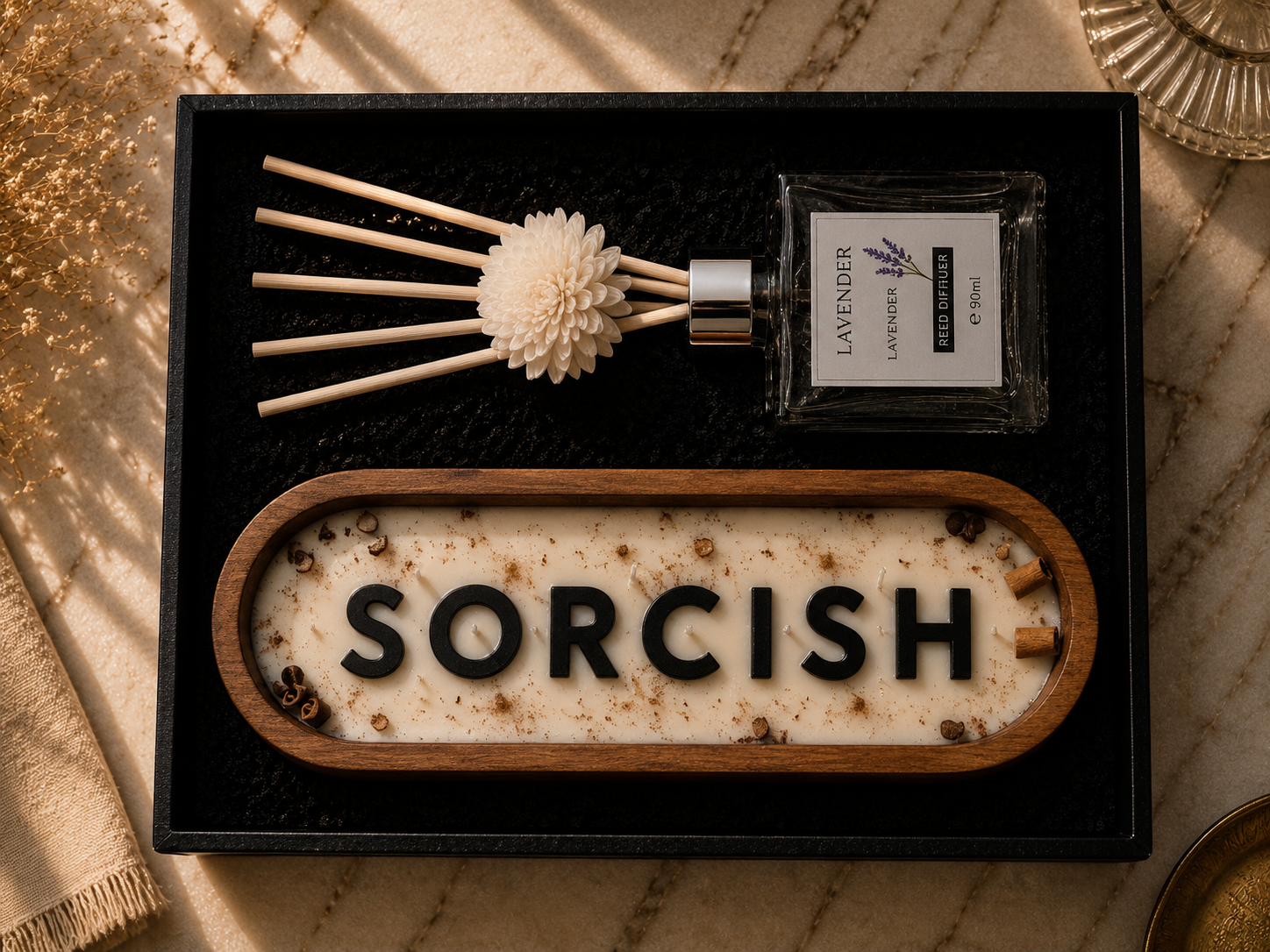 A luxury gift set containing a reed diffuser with a floral reed and a glass bottle labeled 'LAVENDER & LILAC', alongside a wooden oval tray with the word 'SORCISH' spelled in black letters on a cream wax base. The set is presented in a black box on a marble surface with warm, sunlit shadows.