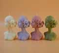 Four woman-shaped candles with floral designs on an orange background
