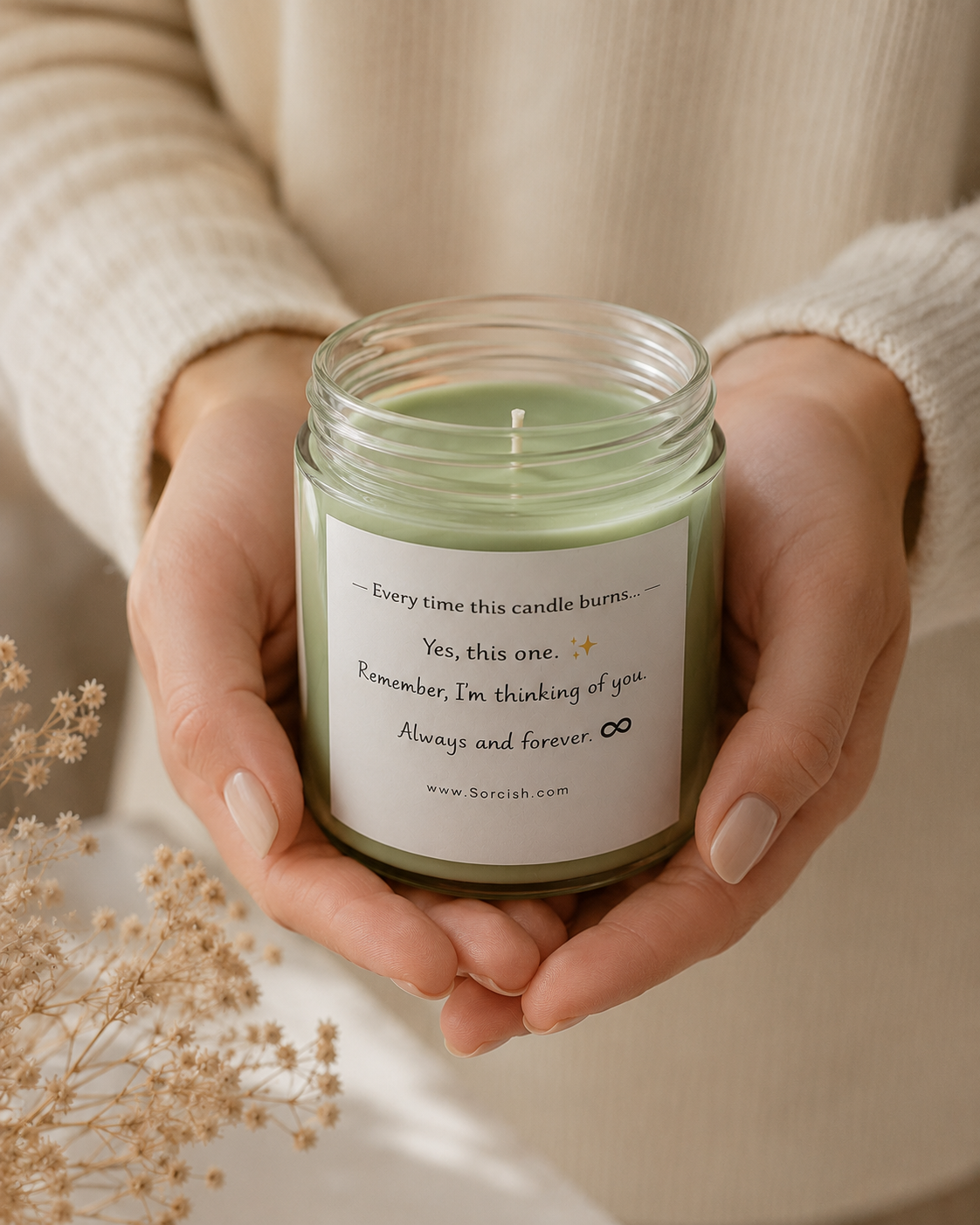 Person holding a candle jar with a message on it, surrounded by dried flowers.