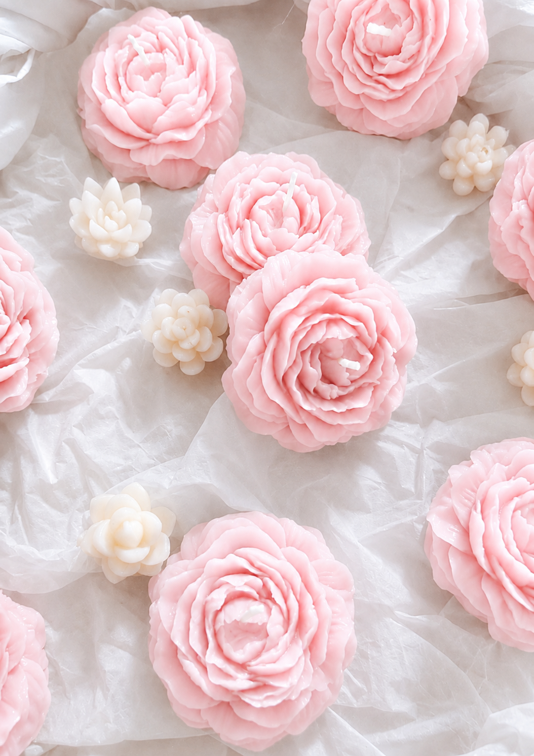 Pink and white artificial flower candles arranged on a crumpled white fabric background.