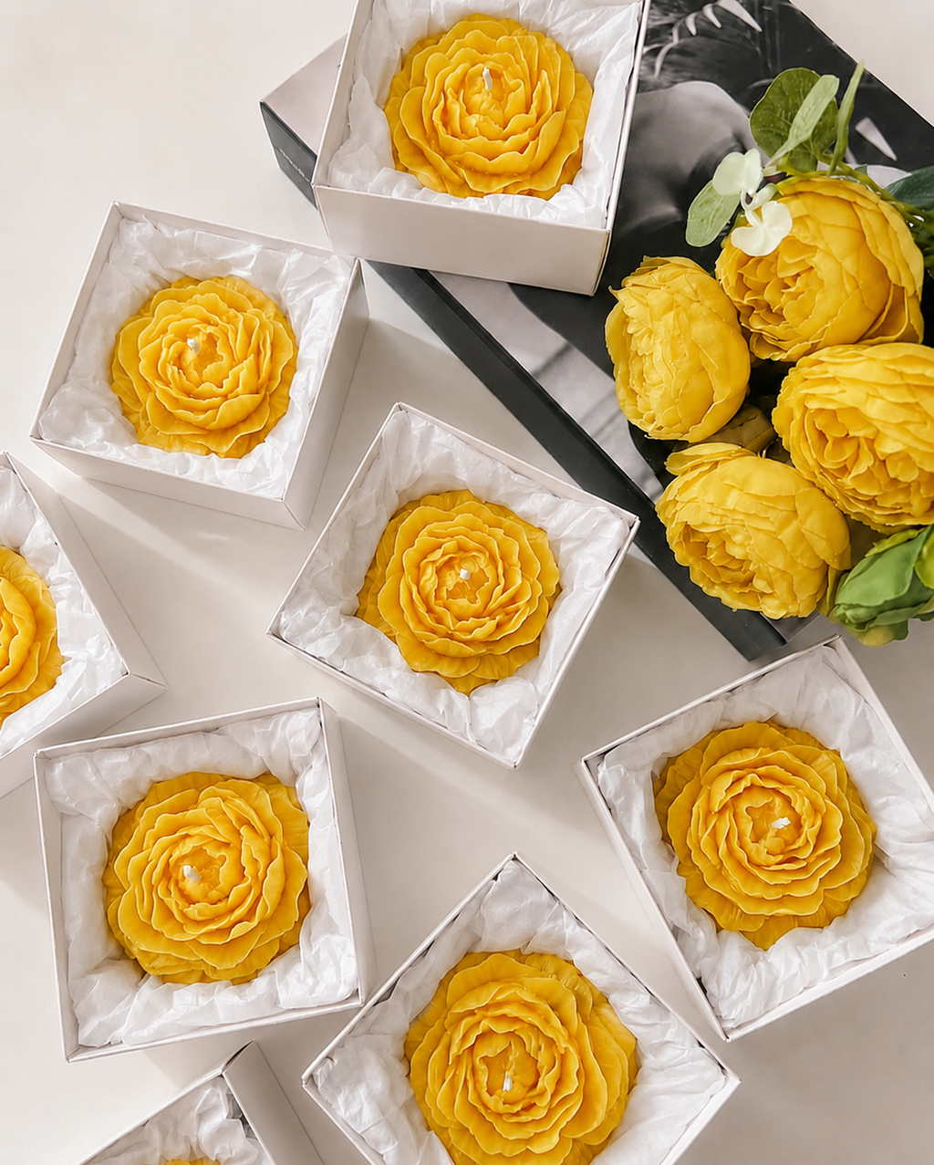 Yellow flower-shaped pastries in white boxes with a bouquet of yellow flowers on a black tray.