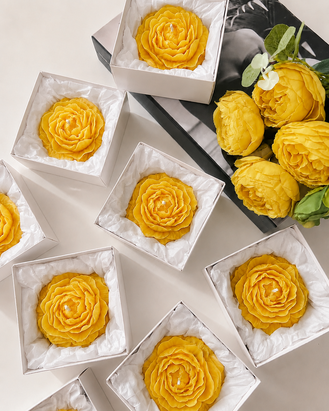 Yellow flower-shaped pastries in white boxes with a bouquet of yellow flowers on a black tray.