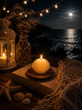 Candle in a shell holder on a book with lantern, flowers, and moonlit sea background