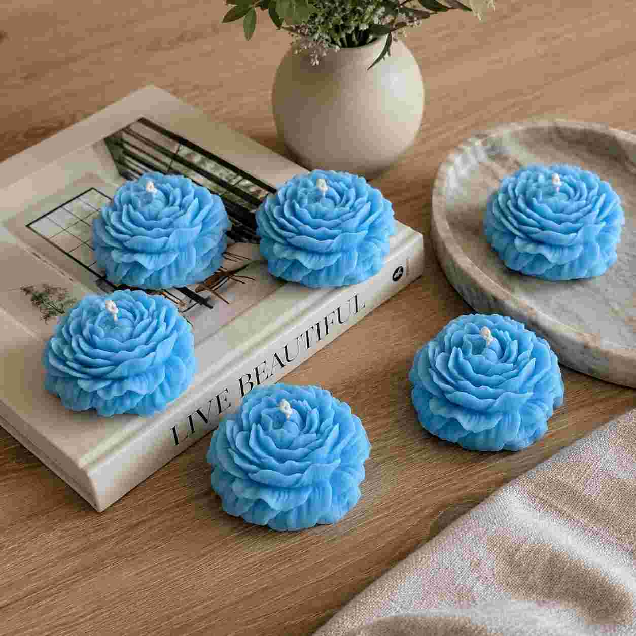 Blue rose-shaped candles on a wooden surface with a book and vase in the background.