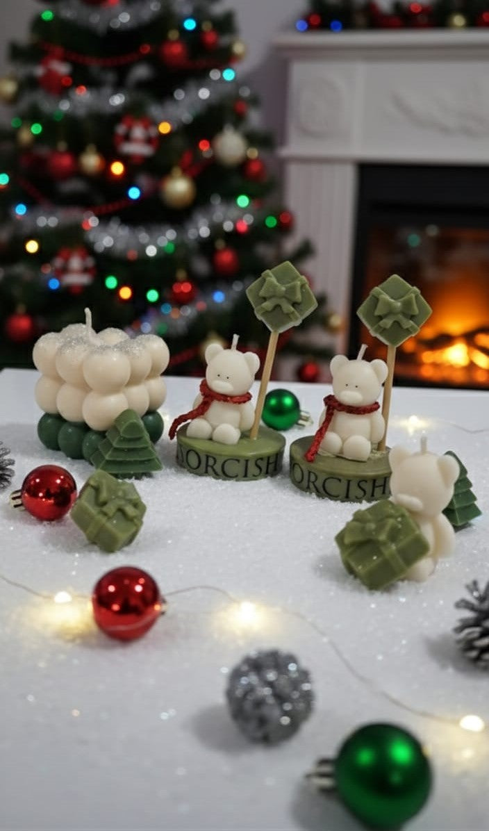 Decorative candles shaped like bears and trees on a table with Christmas decorations in the background.